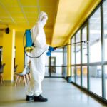 Cleaning and disinfection of office to prevent COVID-19. A disinfection in a protective suit and mask washes office furniture disinfectants. Prevention of spreading pneumonia virus with surfaces.